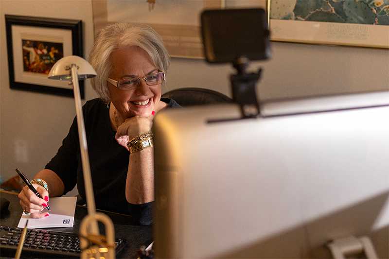 Smiling woman in denim shirt sitting behind her computer